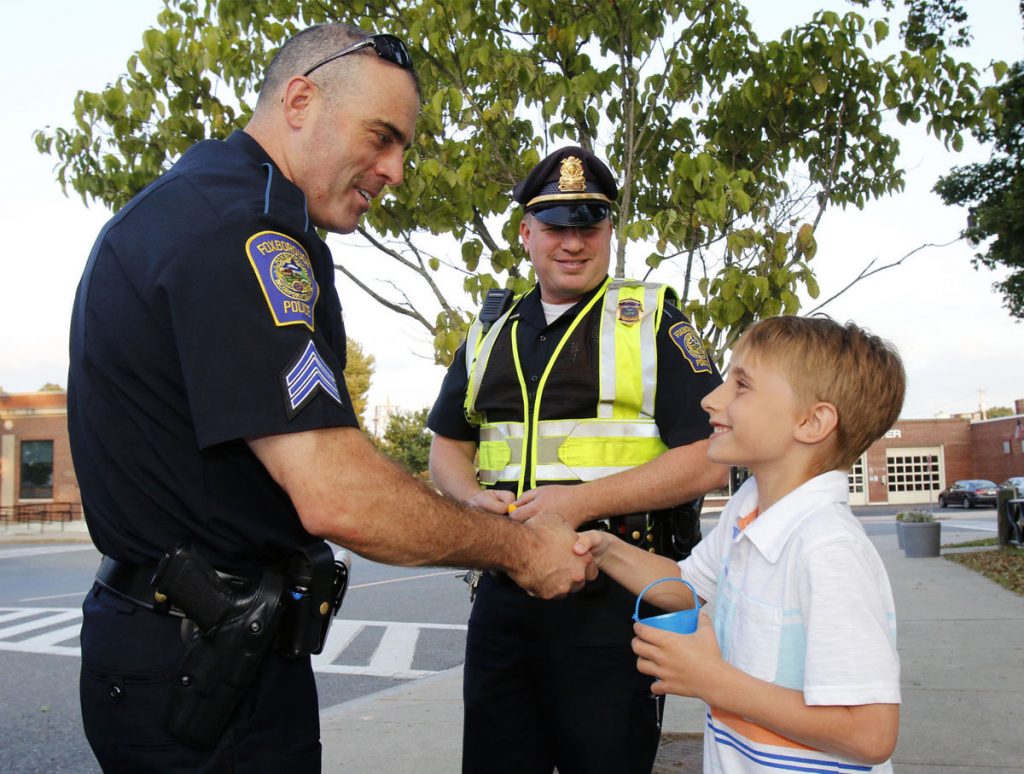 Foxboro Police Sgt. Dave Foscaldo, left, and Lt. Mike Grace are thanked by Ryder Bishop, 8, who presents the officers with a ball representing a good deed. Photo copyright Paul Connors, The Sun Chronicle